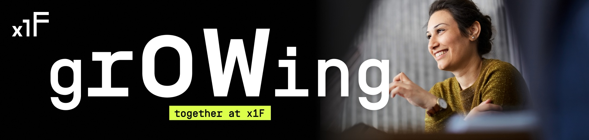 Eine Person sitzt an einem Tisch in einem hellen Raum und spricht etwas mit einer Handbewegung. Links im Bild ist das x1F‑Logo zu sehen. Rechts liegt der große weiße Schriftzug growing über Bild, ergänzt durch das gelbe Textfeld together at x1F.